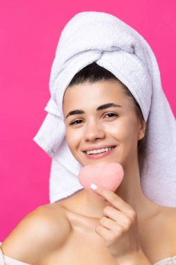 Kafasında havluyla güzel, çekici bir kız, pembe kalp şeklinde bir sünger tutuyor..