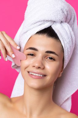 A beautiful cheerful attractive girl with a towel on her head holds a cosmetic heart stone near her face.