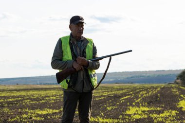 Mature man hunter with gun while walking on field.