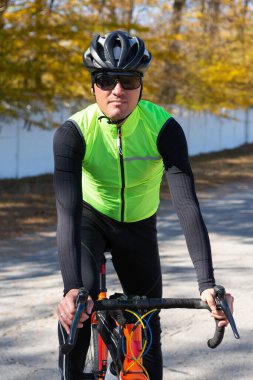 A man in clothes stands with a bicycle on an autumn sunny day. Cyclist in the park.