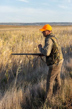 Mature man hunter with gun while walking on field.