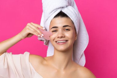 A beautiful cheerful attractive girl with a towel on her head holds a cosmetic heart stone near her face.