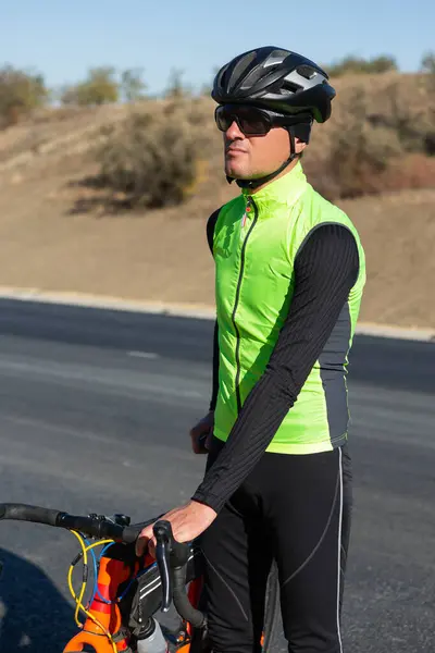 Cyclist riding bicycle on road against clear sky. A man in an outfit stands with a bicycle on an autumn sunny day.