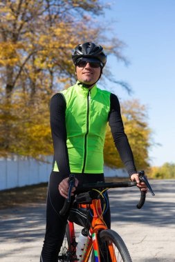 A man in clothes stands with a bicycle on an autumn sunny day. Cyclist in the park.