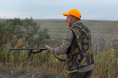 Mature man hunter with gun while walking on field.