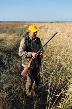 Mature man hunter with gun while walking on field.