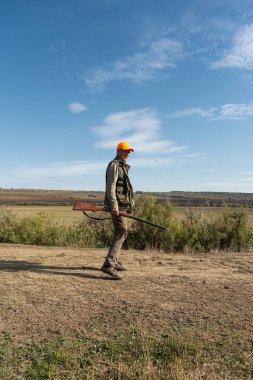 Mature man hunter with gun while walking on field.