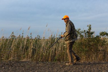 Mature man hunter with gun while walking on field.