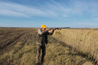 Hunter aiming with rifle while standing against sky