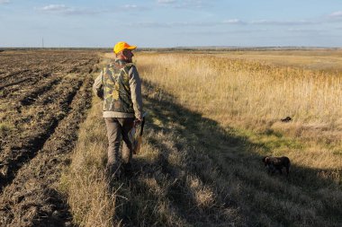 Mature man hunter with gun while walking on field.