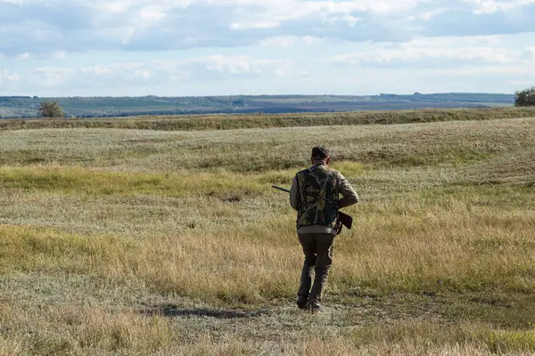 Mature man hunter with gun while walking on field.