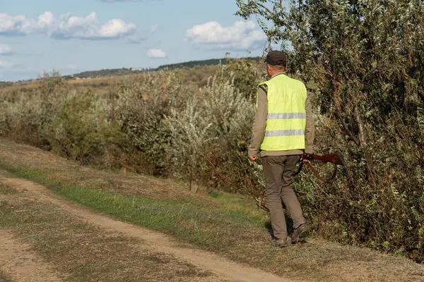Mature man hunter with gun while walking on field.