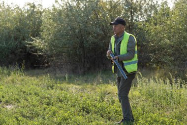 Mature man hunter with gun while walking on field.