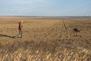 Mature man hunter with gun while walking on field.
