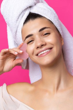 A beautiful cheerful attractive girl with a towel on her head holds a cosmetic heart stone near her face.