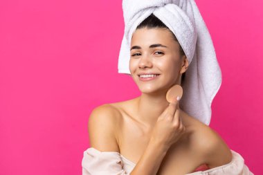 Beautiful cheerful attractive girl with a towel on her head, holds a sponge against a pink background.