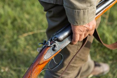 Mature man hunter with gun while walking on field.