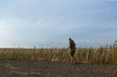 Mature man hunter with gun while walking on field.