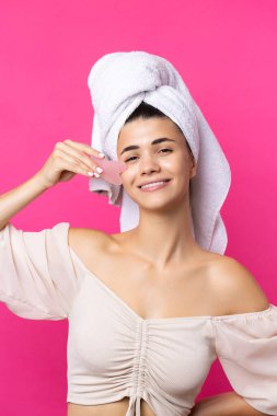 A beautiful cheerful attractive girl with a towel on her head holds a cosmetic heart stone near her face.