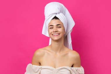 Portrait of young beautiful woman after bath. Beauty face of a cheerful attractive girl with towel on head against a pink background.