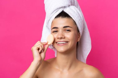 Beautiful cheerful attractive girl with a towel on her head, holds a sponge against a pink background.