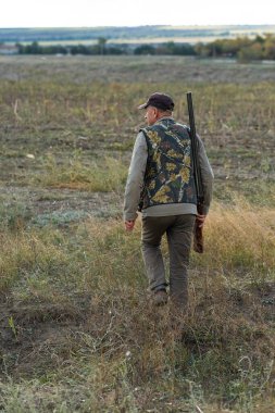 Mature man hunter with gun while walking on field.