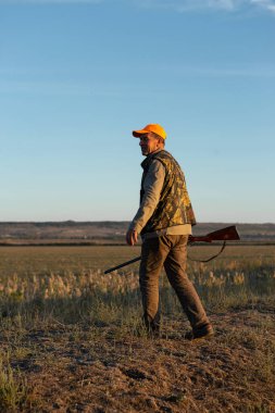 Mature man hunter with gun while walking on field.