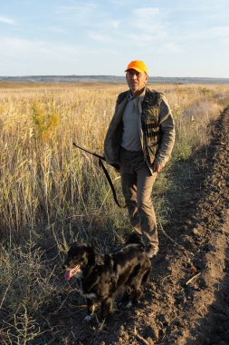 Mature man hunter with gun while walking on field.