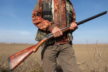 Mature man hunter with gun while walking on field.