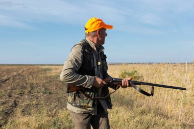 Mature man hunter with gun while walking on field.