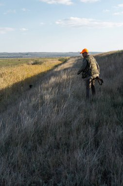 Mature man hunter with gun while walking on field.