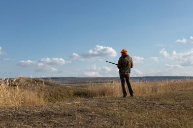 Mature man hunter with gun while walking on field.