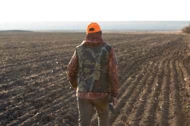 Mature man hunter with gun while walking on field.