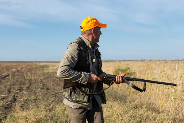 Mature man hunter with gun while walking on field.