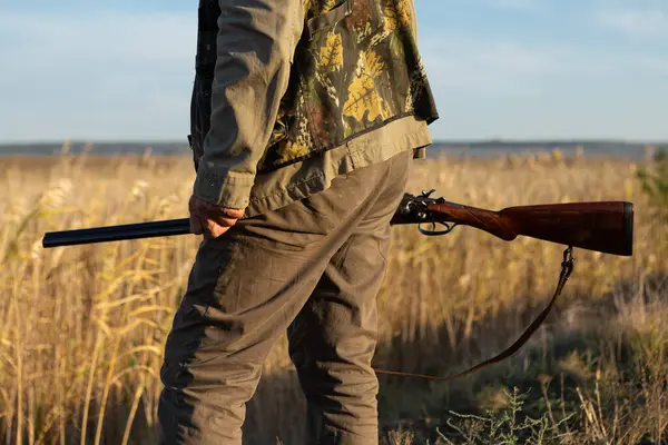 Mature man hunter with gun while walking on field.