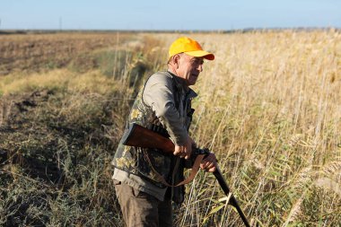 Mature man hunter with gun while walking on field.