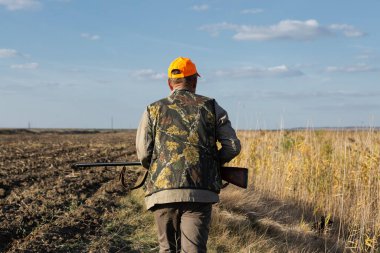 Mature man hunter with gun while walking on field.