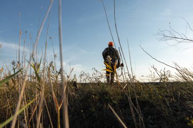 Mature man hunter with gun while walking on field.