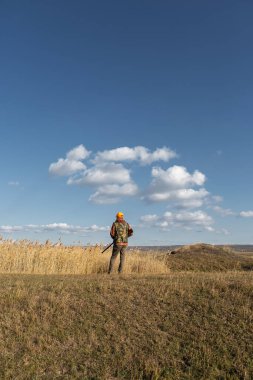 Mature man hunter with gun while walking on field.