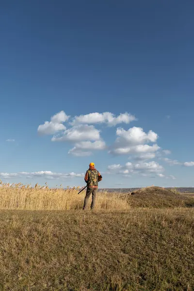 Mature man hunter with gun while walking on field.