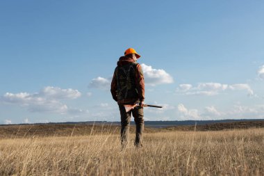 Mature man hunter with gun while walking on field.