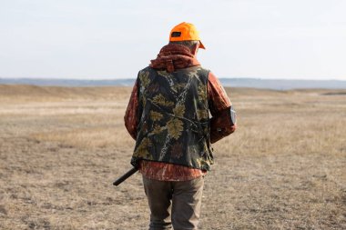 Mature man hunter with gun while walking on field.