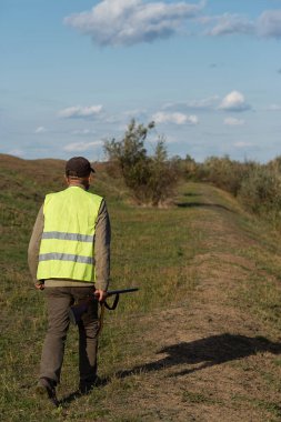 Mature man hunter with gun while walking on field.
