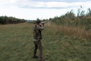 Hunter aiming with rifle while standing against sky 