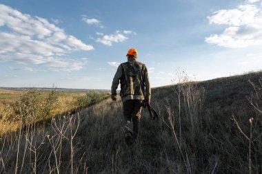 Mature man hunter with gun while walking on field.