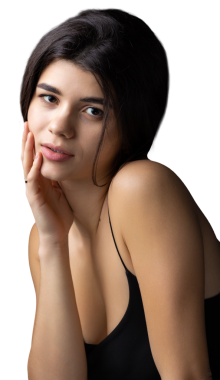 Classic studio portrait of a young brunette dressed in a black top, who is sitting on a chair against a black background.