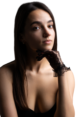Classic dark studio portrait of a young brunette woman in black clothes who is sitting on a chair.