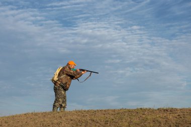 Mature man hunter with gun while walking on field.