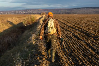 Mature man hunter with gun while walking on field.