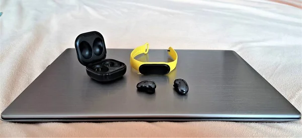 Smart gadgets: metallic laptop, yellow fitness wristband, black buds